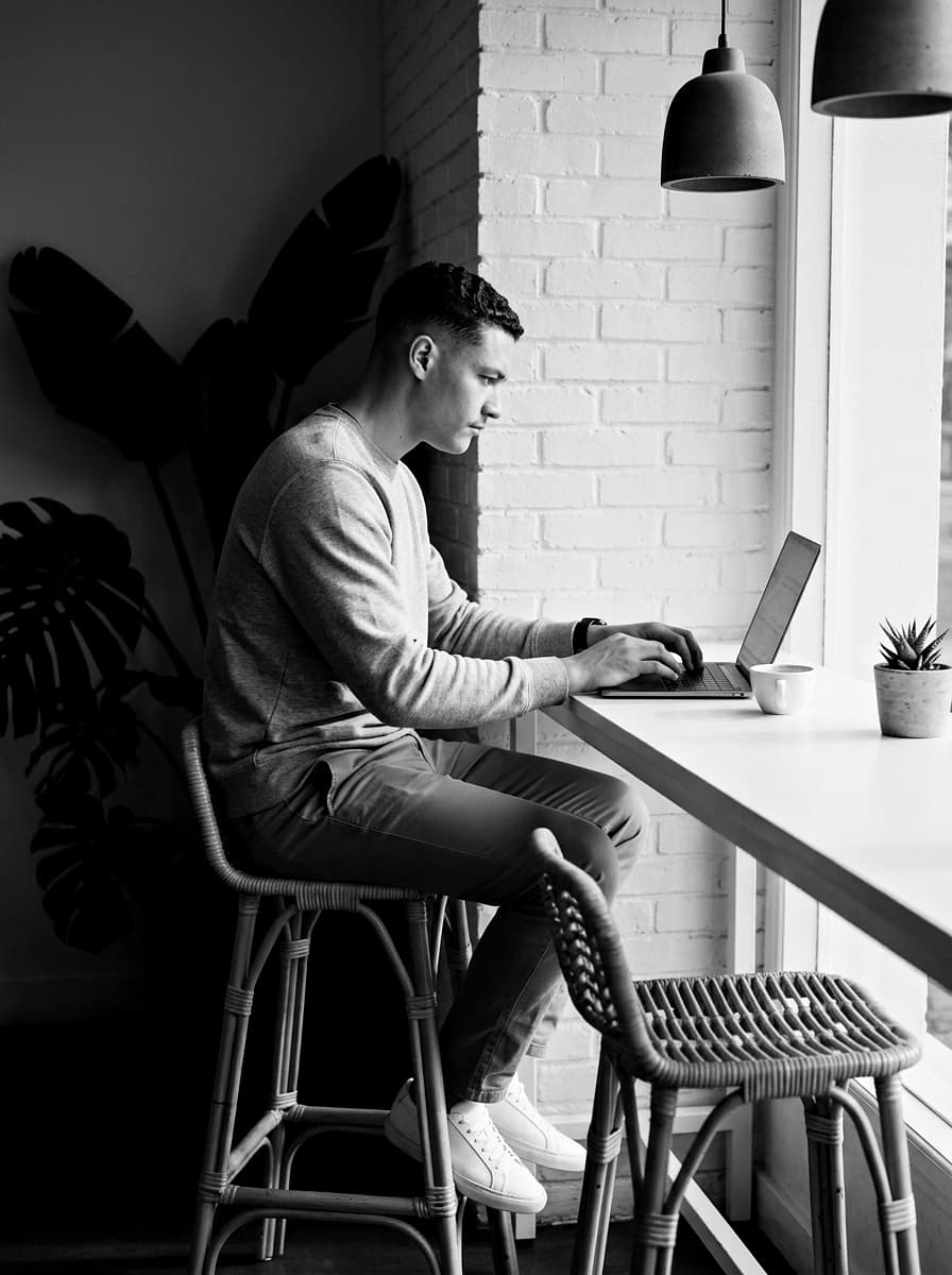 Foto em preto e branco de Matheus trabalhando no notebook em um café